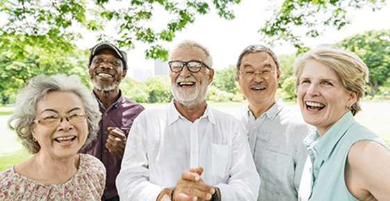 Dr. Luke Fullenkamp : Group of five cheerful senior adults, diverse in ethnicity, laughing and enjoying a sunny day together in a park, despite some having eye conditions.