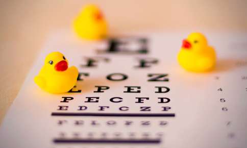 Dr. Luke Fullenkamp : Close-up of an eye chart with rubber ducks out of focus in the background, suggesting a playful vision test concept tailored for infant eye health.